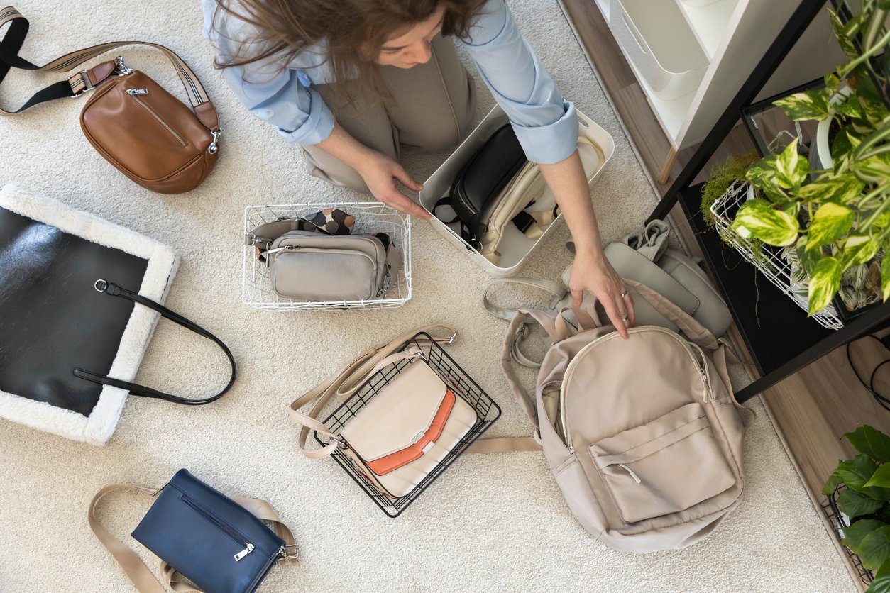 A young woman puts various women's handbags for storage in her home wardrobe. Walk-in closet. Accessories and bags.